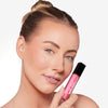 Person holding a pink lip gloss with a black cap, showcasing smooth and radiant skin with a natural makeup look.