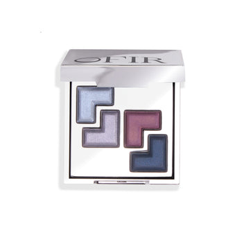 A sleek compact featuring a limited edition collection of four geometric eyeshadow shades in shimmering blue, violet, and dark blue tones, encased in a reflective silver case.