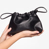 Hand holding a black pouch with drawstring closure against a white background