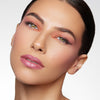 Elegant makeup look featuring soft pink lips, bold winged eyeliner, and a warm peach eyeshadow, complemented by flawless, glowing skin.