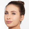 Close-up of woman with flawless skin, subtle makeup, glossy lips, and a neatly styled bun.