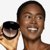 Model holding a bronzer/highlighter product to her face, showcasing a deep shade duo