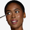 Model holding a rounded point brush near her eyes, showcasing a precision blending brush