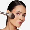 Model holding a thick teardrop shape brush on her cheek, showcasing a multi-use powder brush