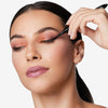 Model holding a liquid eye liner to her eyes, showcasing a black, sharp, and smooth line