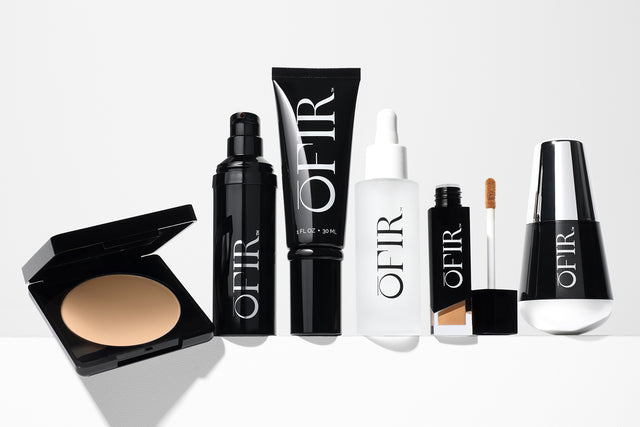 makeup and skincare products displayed on a white background, including a compact powder, a setting spray bottle, hydrating serum, liquid concealer with wand, and a sleek black-and-silver foundation bottle
