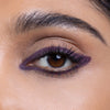 Close-up of an eye with dramatic purple eyeliner and mascara enhancing the lashes, set against smooth, natural skin.