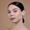 A woman with smooth, glowing skin and sleek, dark hair pulled back, showcasing a natural makeup look on a neutral background.
