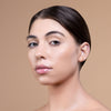 A close-up of a person with smooth, glowing skin and a sleek hairstyle against a neutral background.
