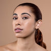 Woman with flawless, glowing skin and natural makeup, showcasing a subtle glossy lip, against a neutral background.