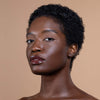 A model with a short afro hairstyle showcases a glossy dark brown lip color and glowing skin on a neutral background.