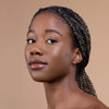 A woman with braided hair and glowing skin looks confidently at the camera against a neutral background, showcasing natural beauty.