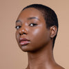 A person with short, textured hair and smooth, natural makeup on a neutral background, showcasing glowing skin.