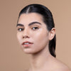 A person with flawless, glowing skin and neatly groomed eyebrows looks confidently at the camera, set against a neutral background.