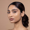 A person with smooth, radiant skin and natural makeup displays a sleek hairstyle against a neutral background, showcasing a beauty look.