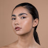 Close-up of a person with flawless, glowing skin and natural makeup, featuring smooth skin texture and soft brown lips, set against a neutral background.