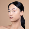 Model showcasing a natural makeup look with a smooth complexion and subtle lip color, set against a neutral background.