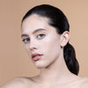 A close-up of a model with clear skin and subtle makeup, featuring a sleek ponytail against a neutral background.