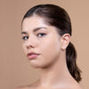 A person with smooth skin and neutral makeup looks confidently towards the camera against a soft beige background.