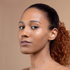 A woman with smooth, glowing skin and pulled-back hair, looking confidently at the camera against a neutral background.