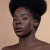 A person with natural afro-textured hair and glossy dark lips poses against a neutral background, highlighting a smooth and radiant complexion.