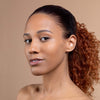 A woman with smooth, glowing skin and natural makeup poses with her hair pulled back, highlighting her clear complexion against a neutral background.