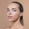 A person with smooth, glowing skin and blue eyes, showcasing a natural makeup look against a neutral background.