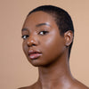 A person with smooth, radiant skin and a short hairstyle showcases a natural makeup look against a neutral background.