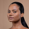 A person with smooth, glowing skin and glossy lips, showcasing a natural makeup look against a neutral background.