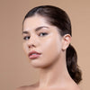 A woman with clear, glowing skin and natural makeup poses against a neutral background, highlighting a smooth complexion and well-defined features.