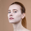 Close-up of a person with a neutral expression and natural makeup, set against a soft beige background.