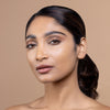 A model with smooth, glowing skin and natural makeup poses against a neutral background, showcasing a beauty look emphasized by understated elegance.