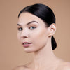 A woman with smooth skin and neatly styled dark hair gazes confidently, showcasing a natural makeup look with defined eyebrows and subtle lip gloss.