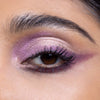Close-up of an eye with purple and pink shimmery eyeshadow, showcasing long lashes and defined eyebrows.