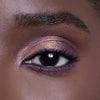 Close-up of an eye with shimmering purple and gold eyeshadow, accentuated by dark lashes and a well-groomed eyebrow.