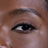 Close-up of a well-groomed eyebrow and eye, showcasing long, voluminous lashes with precise eyeliner application, highlighting a smooth, radiant skin texture.