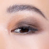 Close-up of an eyelid with a shimmering brown and gold eyeshadow blend, highlighting smooth skin and well-groomed eyebrow.