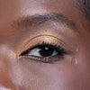 A close-up of an eye with shimmering gold eyeshadow and defined lashes, showcasing a bold makeup look.