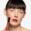 Model holding  a lip gloss and showcasing a red-ish lip color