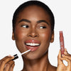 Model applying a warm terracotta pink lip to her lips, showcasing a glossy pink makeup look