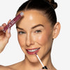 Model applying a rich berry pink lip to her lips, showcasing a glossy pink makeup look