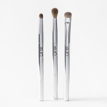 Three OFIR eye brushes with silver handles standing side by side on white background
