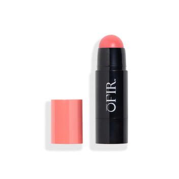 Cream blush stick with a coral-pink cap placed beside the black tube, revealing the rounded blush tip in a matching coral-pink shade. Blank background