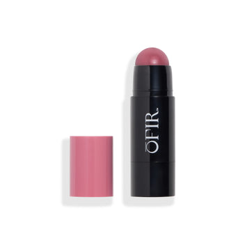 Cream blush stick with a purplish cap placed beside the black tube, revealing the rounded blush tip in a matching purplish shade. Blank background