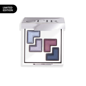 A sleek compact featuring a limited edition collection of four geometric eyeshadow shades in shimmering blue, violet, and dark blue tones, encased in a reflective silver case.