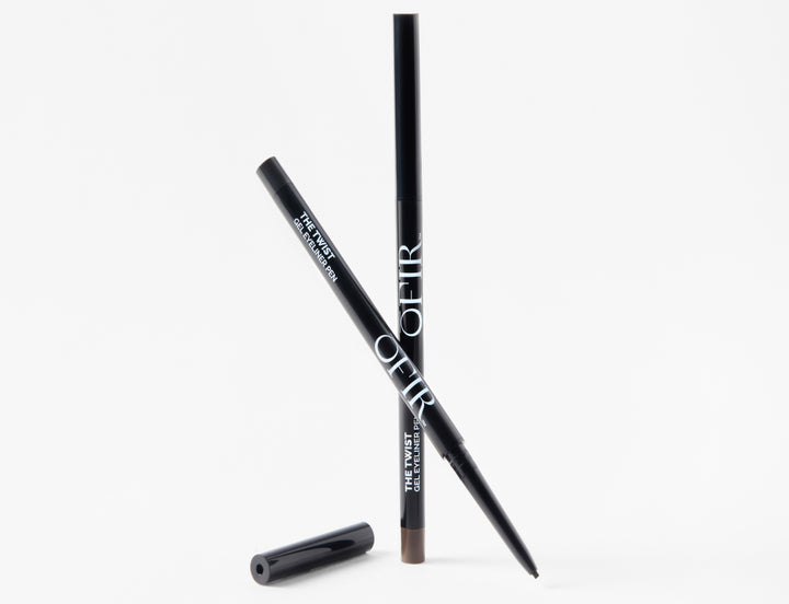 Two OFIR gel eyeliner pens arranged in a crisscross position, one with the cap removed to show the brown gel tip, with the loose cap lying beside them