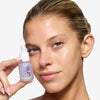 model holding a dropper bottle of OFIR 's Bloom Serum close to her face, showcasing smooth, radiant skin.