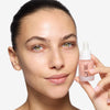 model holding a dropper bottle of OFIR 's Bloom Serum close to her face, showcasing smooth, radiant skin.