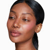 Woman with smooth skin and natural makeup featuring subtle pink blush and glossy lips, hair styled in a sleek back ponytail.