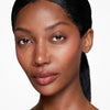 Close-up of a woman with smooth, radiant skin, showcasing natural beauty with subtle makeup and neatly styled hair, set against a neutral background.
